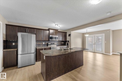 The kitchen features dark wood cabinetry, stainless steel appliances, and a central island with a sink - 84 Calvert Wynd, Fort Saskatchewan, AB - Indoor Photo Showing Kitchen