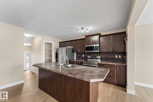 The kitchen features dark wood cabinetry, a double basin sink, and stainless steel appliances, including a microwave, oven, and refrigerator - 84 Calvert Wynd, Fort Saskatchewan, AB - Indoor Photo Showing Kitchen With Double Sink