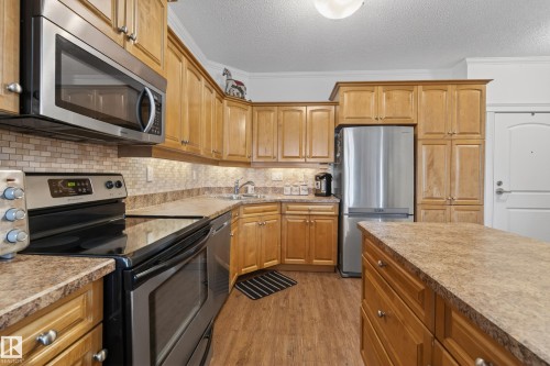 Well-appointed kitchen featuring wood cabinetry, stainless steel appliances, a tiled backsplash, and an island with countertop space - 318 9820 165 Street, Edmonton, AB - Indoor Photo Showing Kitchen