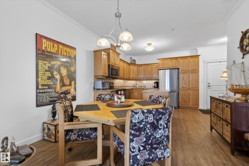 This property features a dining area with wood-style flooring and a kitchen equipped with stainless steel appliances and wood cabinetry - 318 9820 165 Street, Edmonton, AB - Indoor