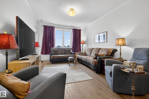 This living area features light-colored walls, wood-look flooring, and a large window providing natural light - 318 9820 165 Street, Edmonton, AB - Indoor Photo Showing Living Room