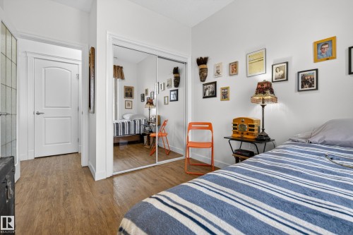 This room features wood-style flooring, a white interior door with an arched panel detail, and a large mirrored closet - 318 9820 165 Street, Edmonton, AB - Indoor Photo Showing Bedroom