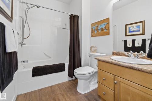 Bathroom featuring a bathtub with an integrated shower, a vanity with a light-colored countertop, and wood-style flooring - 318 9820 165 Street, Edmonton, AB - Indoor Photo Showing Bathroom