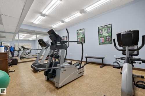 This property features a fitness area with exercise equipment, mirrored walls, and recessed lighting - 318 9820 165 Street, Edmonton, AB - Indoor Photo Showing Gym Room