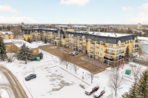 The property features a large building with a yellow exterior and a dark roof, offering balconies and visible parking areas - 318 9820 165 Street, Edmonton, AB - Outdoor With View