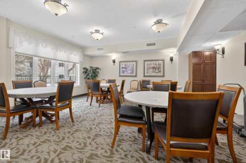 The property features a gathering room with patterned carpeting, several round tables with chairs, and overhead lighting - 318 9820 165 Street, Edmonton, AB - Indoor Photo Showing Dining Room