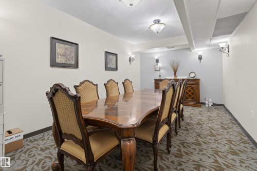 Spacious room featuring a large wooden table with several chairs, patterned carpet, and wall-mounted light fixtures - 318 9820 165 Street, Edmonton, AB - Indoor Photo Showing Dining Room