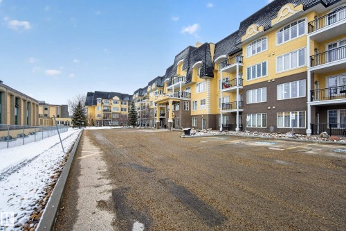 The property features a multi-story building with a yellow and brown exterior, black balconies, and a distinctive black mansard roof - 318 9820 165 Street, Edmonton, AB - Outdoor With Facade