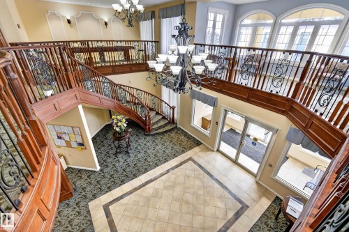 The property features a grand entry with a double staircase, intricate wrought iron and wood railings, and a large chandelier - 318 9820 165 Street, Edmonton, AB - Indoor Photo Showing Other Room