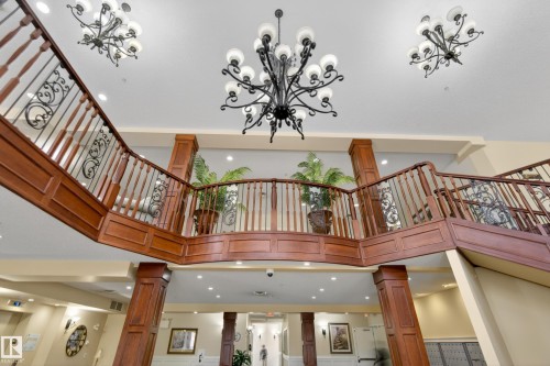 Grand foyer featuring a prominent wooden staircase with wrought iron balusters, complemented by elegant chandeliers and recessed lighting - 318 9820 165 Street, Edmonton, AB - Indoor Photo Showing Other Room