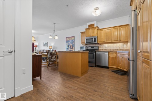The kitchen features wood grain flooring, light wood cabinetry, stainless steel appliances, and a central island with a granite countertop - 318 9820 165 Street, Edmonton, AB - Indoor Photo Showing Kitchen