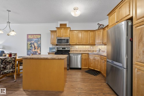 The kitchen features light wood cabinetry, stainless steel appliances, and a central island with a granite countertop - 318 9820 165 Street, Edmonton, AB - Indoor Photo Showing Kitchen