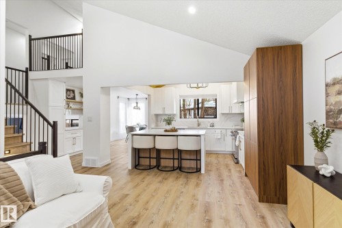 Open concept living space featuring light-toned flooring, a kitchen with white cabinetry and an island, and a staircase with dark railings - 38 Woodcrest Avenue, St. Albert, AB - Indoor Photo Showing Other Room