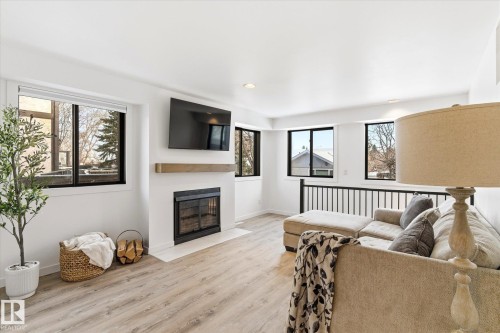 Bright living space featuring light wood-style flooring, a white fireplace with a natural wood mantle, and dark-framed windows - 38 Woodcrest Avenue, St. Albert, AB - Indoor Photo Showing Living Room With Fireplace