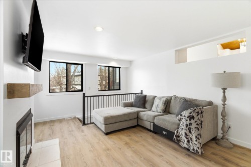 Living room featuring light wood flooring, a fireplace with a light-colored hearth, and two windows providing natural light - 38 Woodcrest Avenue, St. Albert, AB - Indoor Photo Showing Other Room