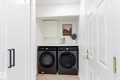 The laundry area features a white countertop, a white wall cabinet, and dark-colored washer and dryer units - 38 Woodcrest Avenue, St. Albert, AB - Indoor Photo Showing Laundry Room