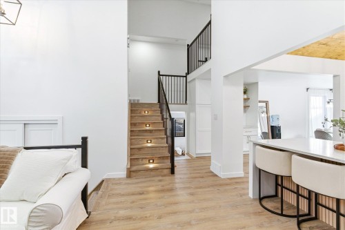 Open concept living space featuring light wood flooring, a staircase with integrated lighting and black metal railings, and a kitchen island with seating - 38 Woodcrest Avenue, St. Albert, AB - Indoor