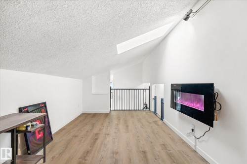 The property features a spacious room with hardwood flooring, high vaulted ceilings, and a wall-mounted electric fireplace - 38 Woodcrest Avenue, St. Albert, AB - Indoor Photo Showing Other Room