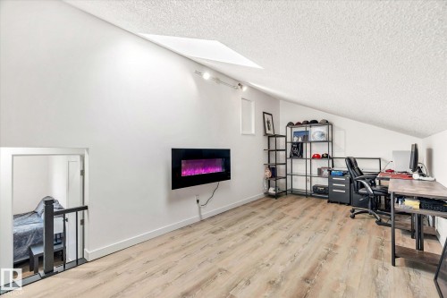Versatile loft area featuring light wood-look flooring, a modern wall-mounted fireplace, and an angled ceiling with track lighting - 38 Woodcrest Avenue, St. Albert, AB - Indoor