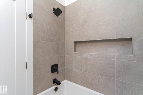 Bathroom featuring a white bathtub, matte black fixtures, a tiled wall, and an integrated shower niche - 38 Woodcrest Avenue, St. Albert, AB - Indoor Photo Showing Bathroom