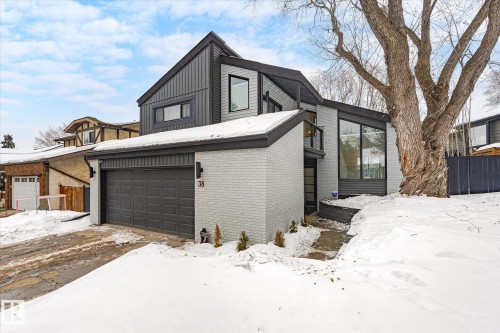 Contemporary property with a striking dark and light gray exterior, featuring a gray garage door, a prominent front window, and a large mature tree in the front yard - 38 Woodcrest Avenue, St. Albert, AB - Outdoor