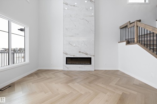 Inviting living space featuring light-colored herringbone-patterned flooring, a tall fireplace with a marble-like surround, and a large window providing views of the surrounding area - 236 Kinglet Boulevard Nw, Edmonton, AB - Indoor With Fireplace