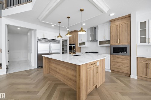 The kitchen features a large island with a white countertop and gold-toned pendant lighting, complemented by a combination of light wood and white cabinetry - 236 Kinglet Boulevard Nw, Edmonton, AB - Indoor Photo Showing Kitchen With Upgraded Kitchen