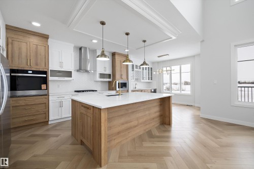 The kitchen features modern cabinetry in both natural wood and white finishes, stainless steel appliances, and a central island with a white countertop - 236 Kinglet Boulevard Nw, Edmonton, AB - Indoor Photo Showing Kitchen With Upgraded Kitchen