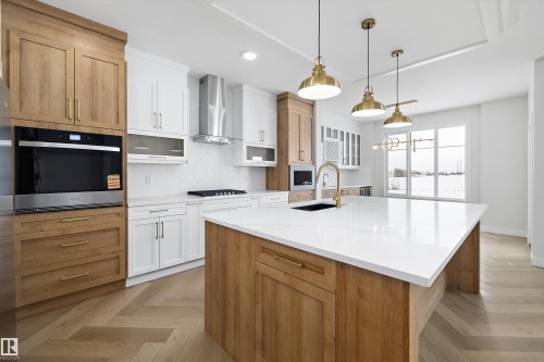 Contemporary kitchen featuring an expansive island with a white countertop and a built-in sink, warm wood cabinetry, and white overhead cabinets - 236 Kinglet Boulevard Nw, Edmonton, AB - Indoor Photo Showing Kitchen