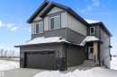 The property features a two-story exterior with a contrasting grey and light grey siding, a front-facing garage with paneling, and a covered entry with white steps - 236 Kinglet Boulevard Nw, Edmonton, AB  - Outdoor 