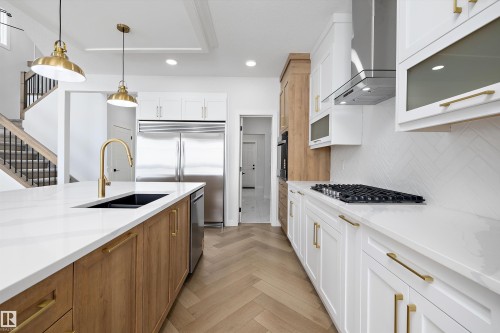 The kitchen features a large island with a black sink and brass faucet, stainless steel appliances, and herringbone pattern hardwood flooring - 236 Kinglet Boulevard Nw, Edmonton, AB - Indoor Photo Showing Kitchen With Double Sink With Upgraded Kitchen