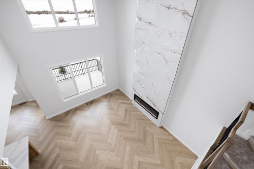 This spacious room features herringbone wood flooring, a tall fireplace with a marble-like finish, and large windows that provide abundant natural light - 236 Kinglet Boulevard Nw, Edmonton, AB - Indoor Photo Showing Other Room