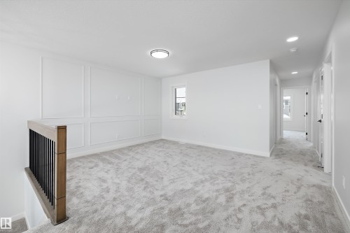 Spacious landing area featuring light gray carpeting, wainscoting details on the wall, and a large window providing natural light - 236 Kinglet Boulevard Nw, Edmonton, AB - Indoor Photo Showing Other Room