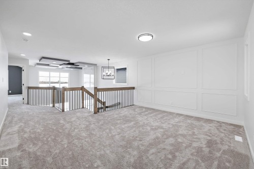 Spacious carpeted area featuring white walls, decorative wall molding, and a modern ceiling light fixture - 236 Kinglet Boulevard Nw, Edmonton, AB - Indoor Photo Showing Other Room