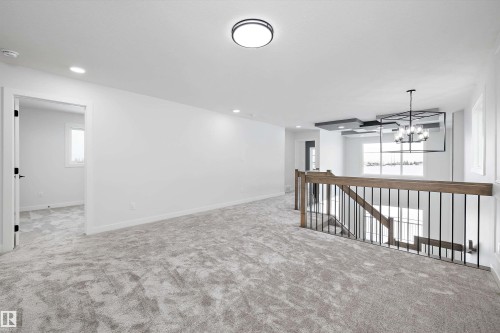 Spacious upper level with neutral carpeting and white walls, featuring a wooden and black iron baluster railing, and a contemporary chandelier - 236 Kinglet Boulevard Nw, Edmonton, AB - Indoor Photo Showing Other Room
