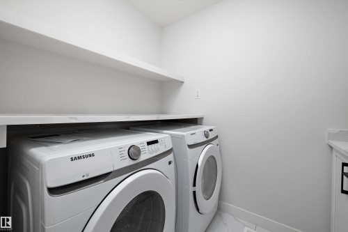 Dedicated laundry area with a white front-load washer and dryer, complemented by a white floating shelf and countertop space - 236 Kinglet Boulevard Nw, Edmonton, AB - Indoor Photo Showing Laundry Room