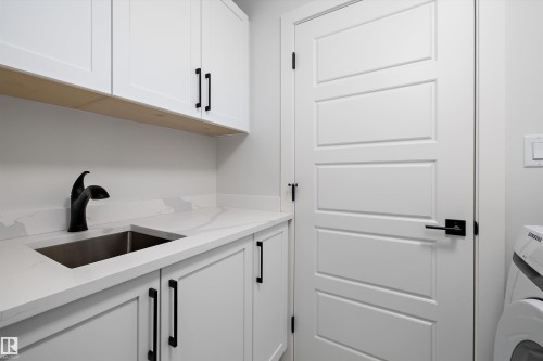 The laundry area features white cabinetry with black hardware, a stainless steel sink, and light-colored countertops - 236 Kinglet Boulevard Nw, Edmonton, AB - Indoor Photo Showing Laundry Room