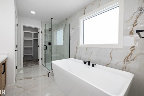 Bathroom featuring a freestanding tub with black fixtures, a glass-enclosed shower, and a window providing natural light - 236 Kinglet Boulevard Nw, Edmonton, AB - Indoor Photo Showing Bathroom