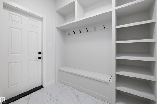Entryway featuring white six-panel door with black hardware, built-in shelving, storage bench, and wall hooks, all set against a light-toned tiled floor - 236 Kinglet Boulevard Nw, Edmonton, AB - Indoor With Storage