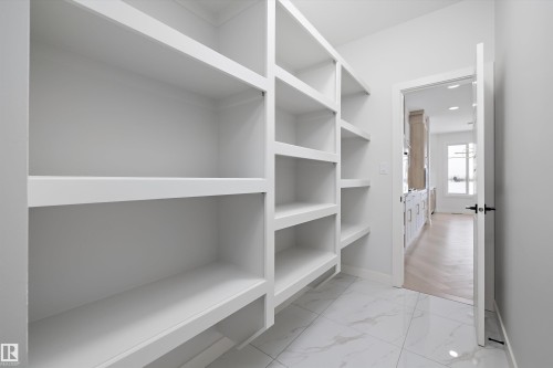 Spacious pantry featuring extensive built-in shelving, white marble-look floor tiles, and a doorway opening to additional living areas - 236 Kinglet Boulevard Nw, Edmonton, AB - Indoor With Storage