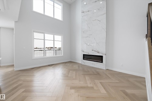 Living area featuring light wood flooring in a herringbone pattern, a tall fireplace with a white marble-look surround, and high ceilings - 236 Kinglet Boulevard Nw, Edmonton, AB - Indoor Photo Showing Other Room With Fireplace