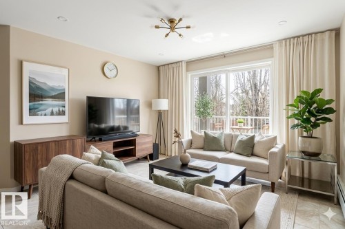 The living area features a large sliding glass door, a modern light fixture, and a built-in media console - 224 3425 19 Street Nw, Edmonton, AB - Indoor Photo Showing Living Room
