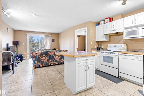 Open-concept living area featuring tile flooring, a kitchen with white cabinetry and appliances, and a sliding glass door leading to an outdoor space - 224 3425 19 Street Nw, Edmonton, AB - Indoor Photo Showing Kitchen