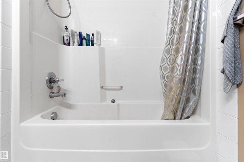 The bathroom features a white bathtub with a shower and a contemporary shower curtain - 224 3425 19 Street Nw, Edmonton, AB - Indoor Photo Showing Bathroom