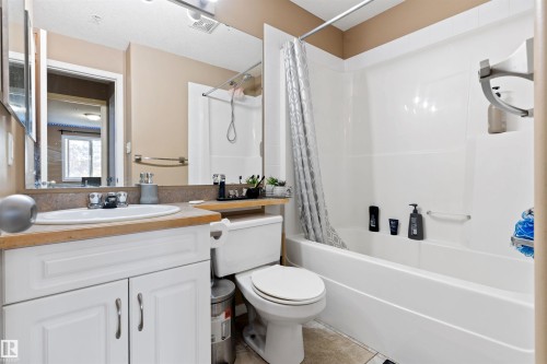 Bathroom featuring a white vanity with a single sink, an integrated bathtub and shower, and a large mirror - 224 3425 19 Street Nw, Edmonton, AB - Indoor Photo Showing Bathroom