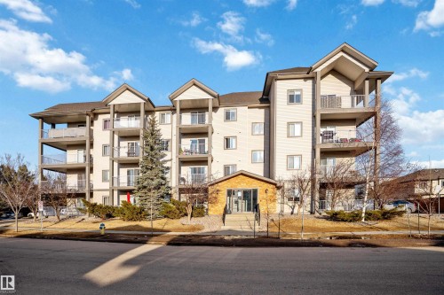 The property features a multi-story building with a light-colored exterior and dark roof, including several balconies with railings - 224 3425 19 Street Nw, Edmonton, AB - Outdoor With Facade