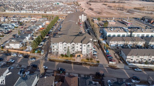 A large apartment building with balconies, surrounded by residential homes and streets, with commercial buildings visible in the distance - 224 3425 19 Street Nw, Edmonton, AB - Outdoor With View