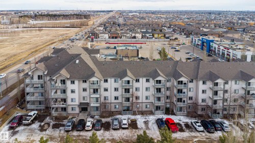 The property is a low-rise condominium building featuring balconies, a parking area, and a grey shingled roof - 224 3425 19 Street Nw, Edmonton, AB - Outdoor With Facade