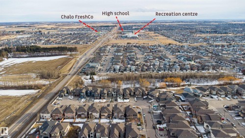 Aerial view showcasing the surrounding residential area with houses featuring dark roofs, roads, and a commercial building - 224 3425 19 Street Nw, Edmonton, AB - Outdoor With View
