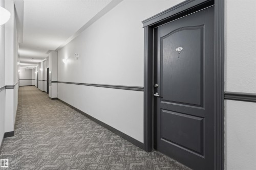 The property features a dark-paneled entry door with a door number, set within a well-lit hallway - 224 3425 19 Street Nw, Edmonton, AB - Indoor Photo Showing Other Room